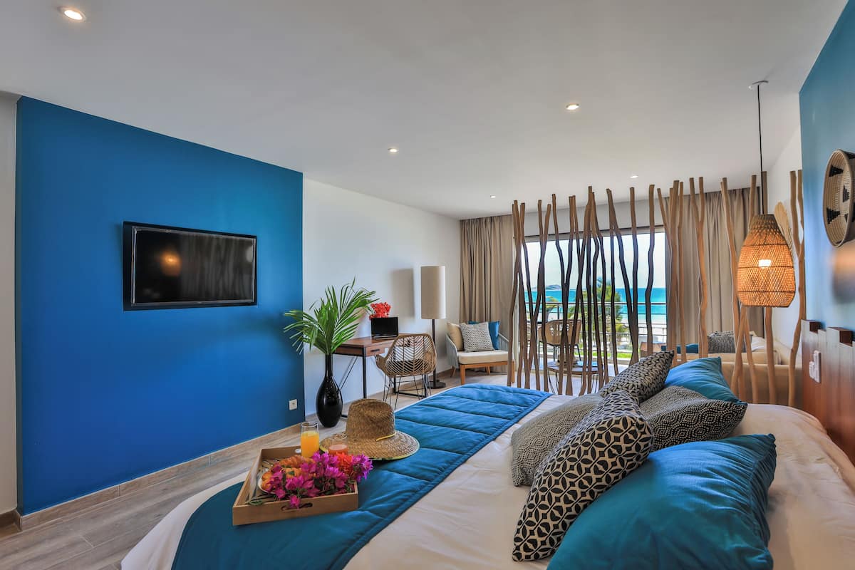 A modern hotel room with a large bed, a desk, a chair, and a view of the ocean.