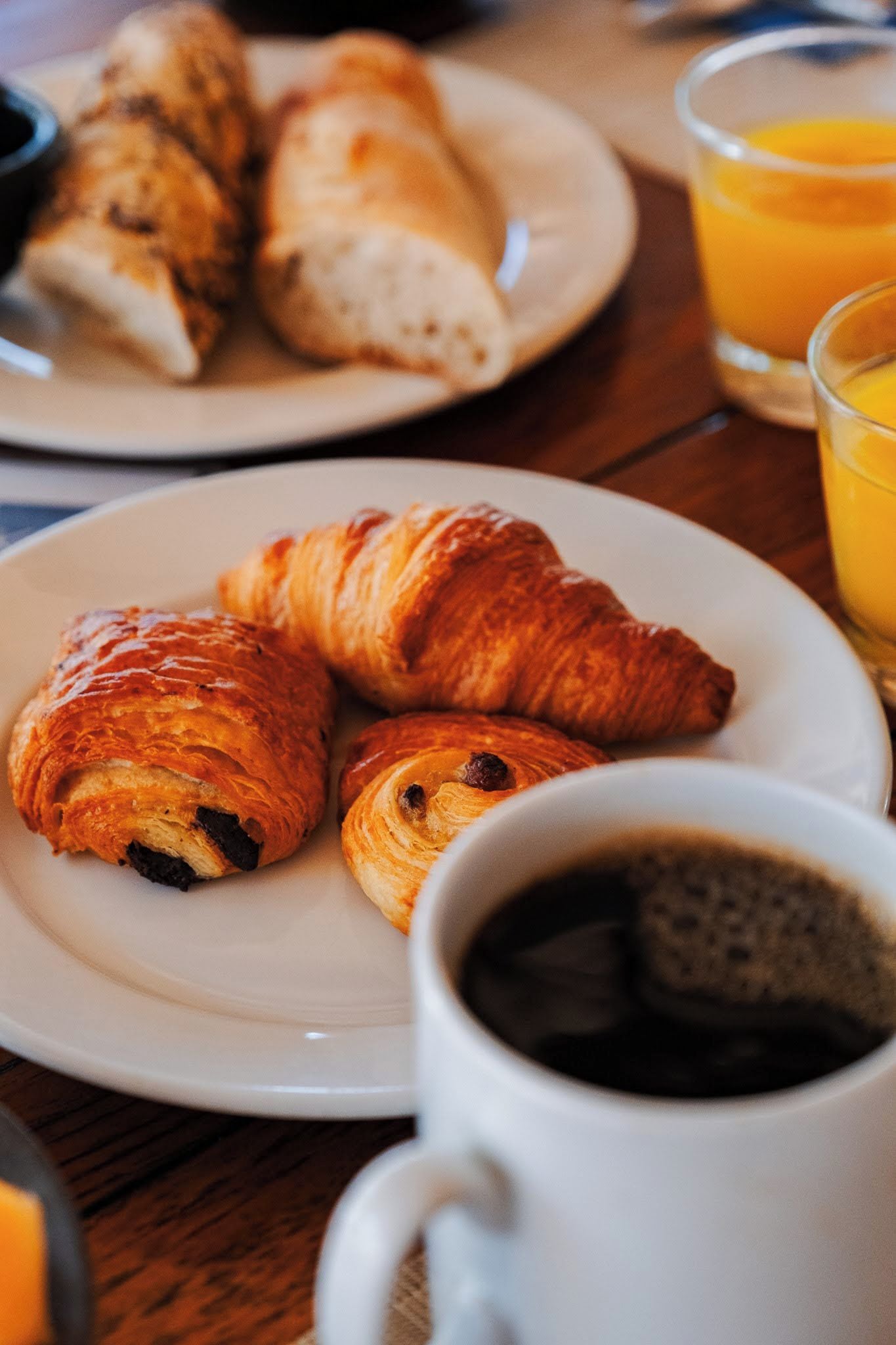 A breakfast setting with croissants, a cup of coffee, and a glass of orange juice on a wooden table.