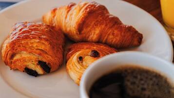 A breakfast setting with croissants, a cup of coffee, and a glass of orange juice on a wooden table.