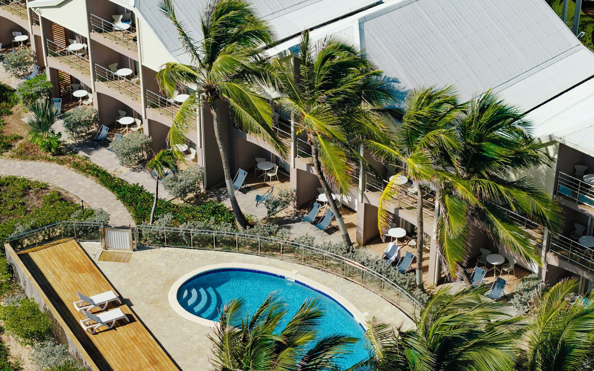 A multi-level hotel with a swimming pool, outdoor seating, and palm trees.