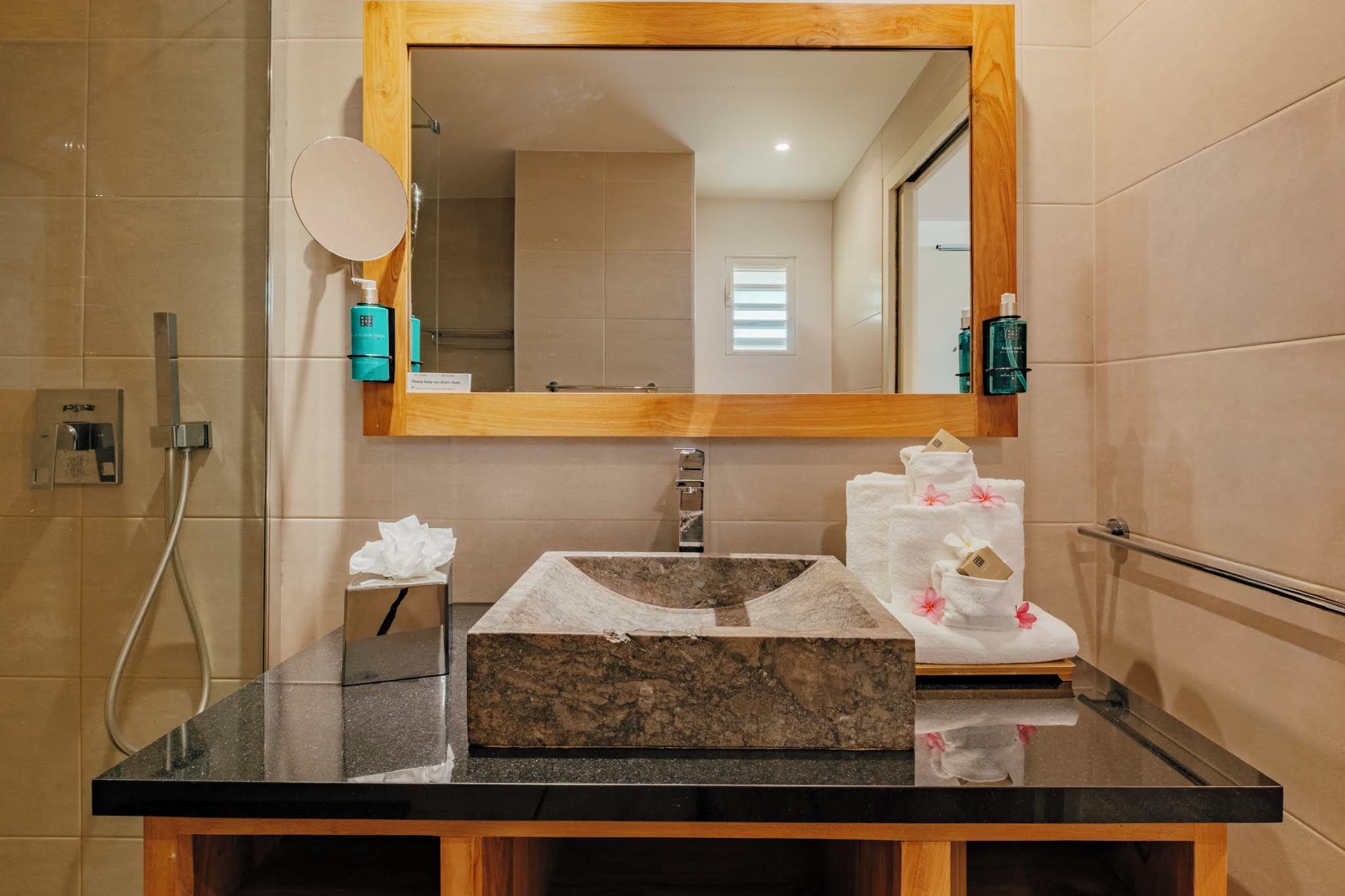 Un bagno con un lavandino in marmo, uno specchio, un portasciugamani con asciugamani e una zona doccia.