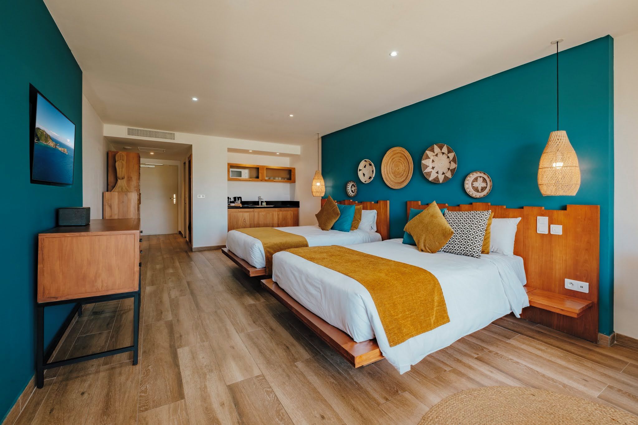 A hotel room with two beds, a wooden desk, a kitchenette, and a view of the sea.