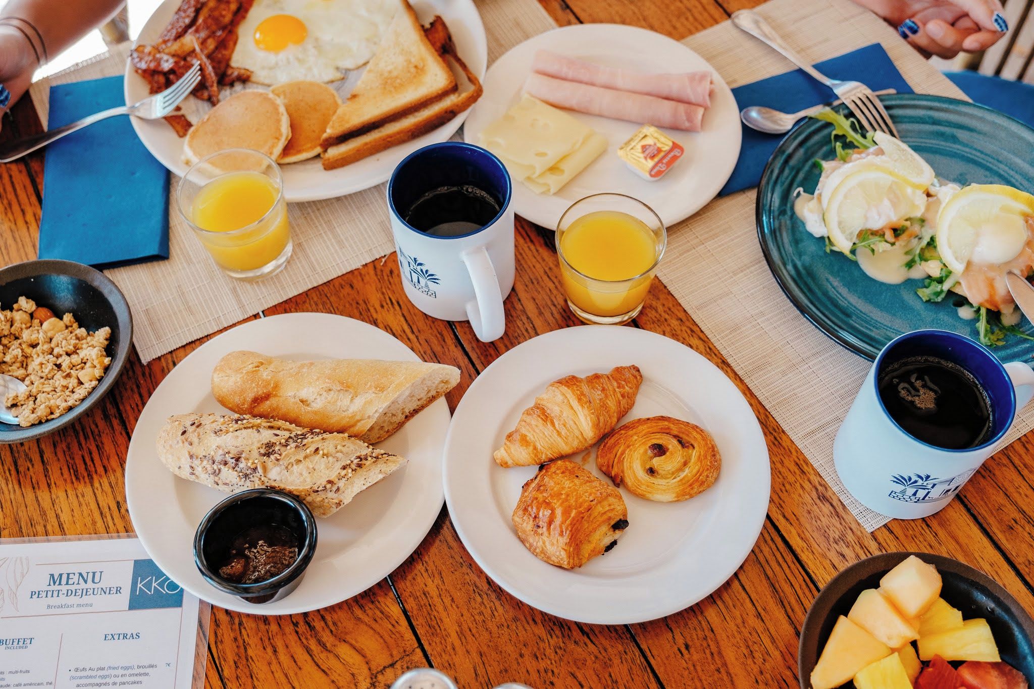 Une table de petit-déjeuner avec des assiettes d’œufs, de pain grillé, de croissants et des fruits.