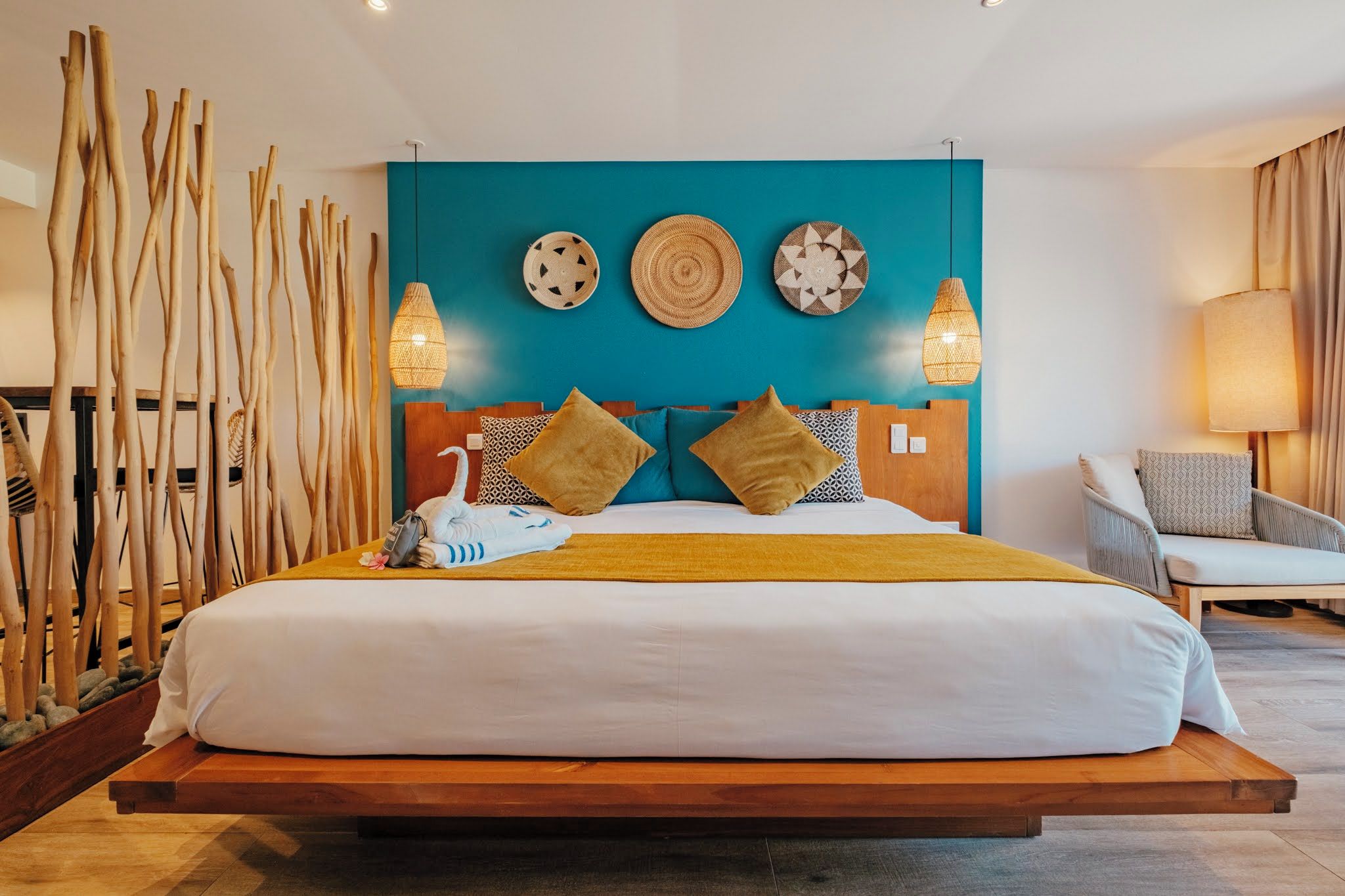Una cama grande con estructura de madera, una pared de acento color turquesa y tres lámparas fijadas a la pared.