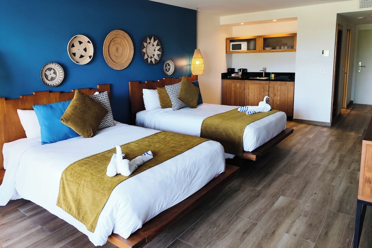 A hotel room with two beds, a kitchenette, and decorative wall art.