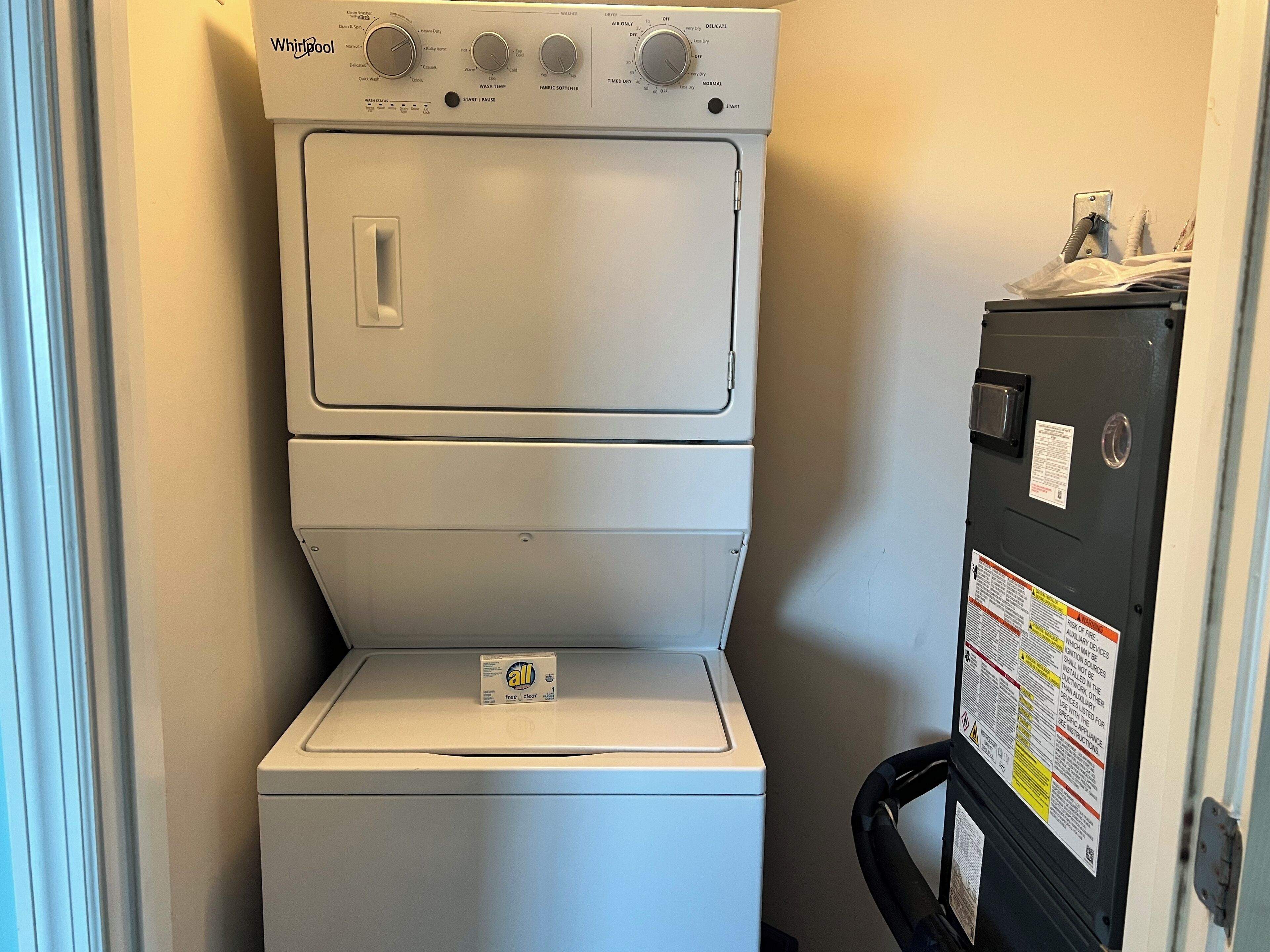 A front-loading Whirlpool washer and dryer unit with a control panel, a detergent box, and a safety label on the door.