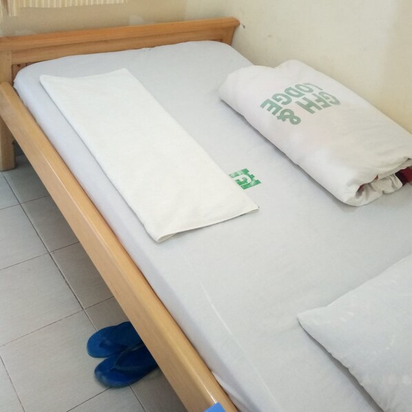Ein Einzelbett mit Holzrahmen, weißer Bettwäsche und einem grünen Logo auf dem Kopfkissen.