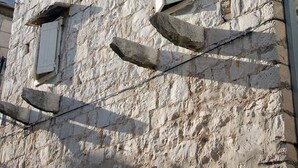 Un edificio de piedra con aspecto rústico, que presenta una escalera de madera que lleva a una ventana con contraventanas.