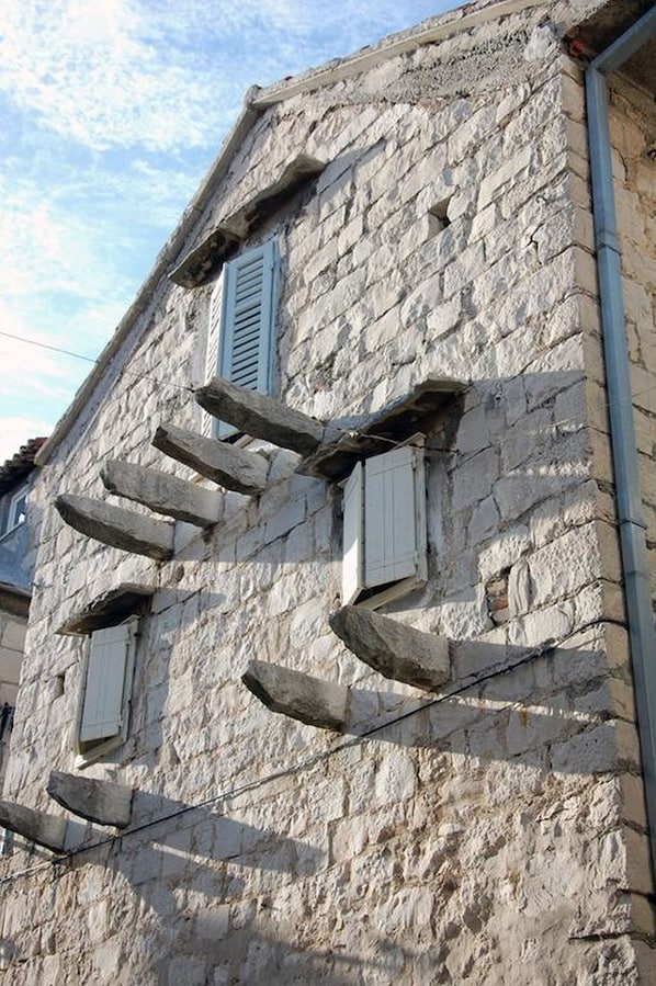 A stone building with a rustic appearance, featuring a wooden staircase leading to a window with shutters.