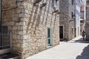 Une rue étroite bordée d’immeubles en pierre, avec une grille en métal et une personne qui marche.