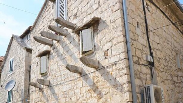 Un edificio de piedra con una escalera que lleva a la entrada, una antena parabólica y un equipo de aire acondicionado.