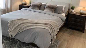 Un dormitorio con cama, mesitas de noche, ventilador de techo y ventana con cortinas.