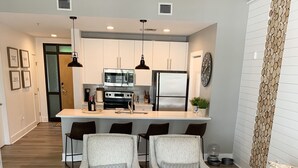A modern living room with a central coffee table, two armchairs, a sofa, and a kitchen in the background.