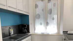 A modern kitchen with white cabinets, a blue accent wall, a coffee maker, and a window with blinds. - Calm and relaxation in Champagne (Verneuil)