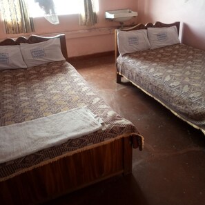 Dos camas de madera con ropa de cama y almohadas estampadas, una ventana con cortinas y un lavamanos fijado a la pared.