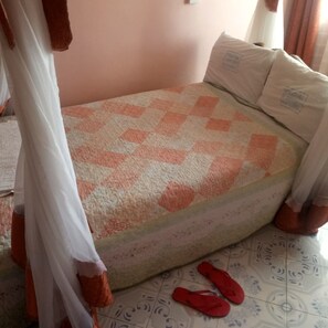 Un dormitorio con una colcha a cuadros, almohadas, una cama, una cortina y un par de zapatillas en el suelo.