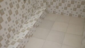 Une salle de bain dont le sol et les murs sont recouverts de carrelage, et qui comprend un banc le long d’un des murs.