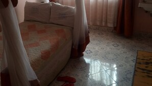 Une chambre à coucher avec un lit, une table de chevet, une fenêtre avec des rideaux et un plancher carrelé.