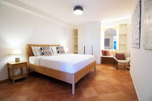 Quarto com cama de madeira, mesa de cabeceira com luminária, uma cadeira e guarda-roupa.