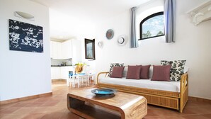 Una sala de estar con una mesa de centro de madera, un sofá con cojines estampados y una cocina al fondo.
