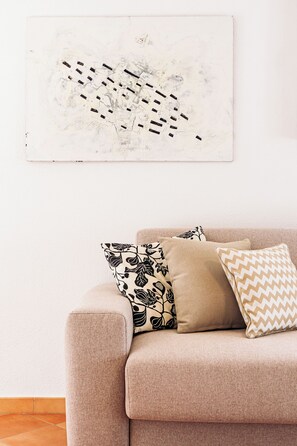 A living room with a beige sofa, two patterned pillows, and a large abstract painting on the wall.