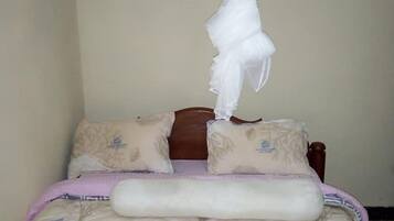 Una cama con dosel, varios cojines y una colcha con estampado de árboles.