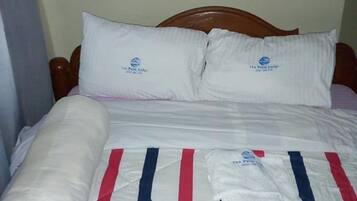 Una cama con colchón blanco y una colcha a rayas rojas y azules. Hay dos almohadas con un logotipo.