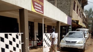 A man walking past a building with a sign for 'Midtown Hotel' offering amenities like meals, accommodation, and conference facilities. - Bungoma Midtown Hotel (Bungoma)