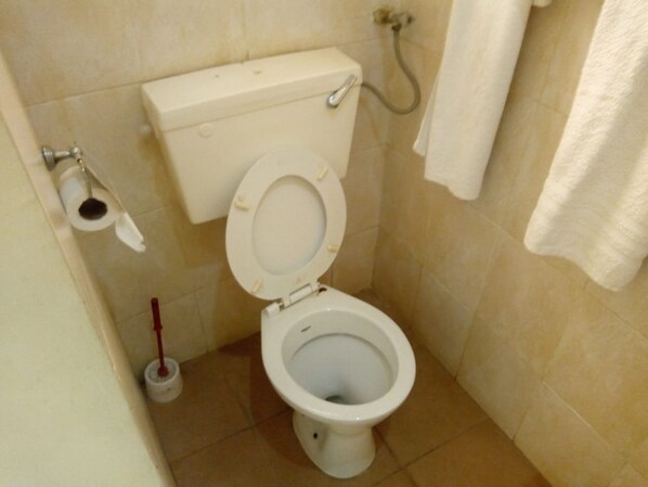A small bathroom with a toilet, a toilet paper holder, a bidet, and a towel hanging on the wall. - Bungoma Midtown Hotel (Bungoma)
