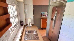 Cuina amb un rentaplat, un ventilador, un frigorífic i un tamboret de fusta.