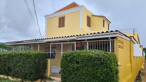 Edifici groc amb teulada de rajola, entrada tancada amb reixatge i dues finestres amb persianes.