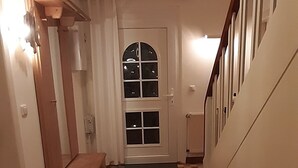 En gang med skakternet gulv, en træbænk, en dør med et vindue og en trappe.