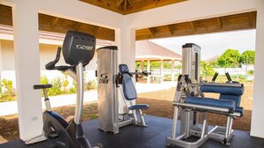 Un gimnasio al aire libre cubierto equipado con una bicicleta estática, una máquina de pesas y una banca.