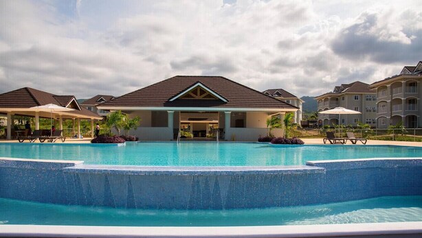 Una piscina con cubierta de madera, rodeada de edificios con un patio techado.