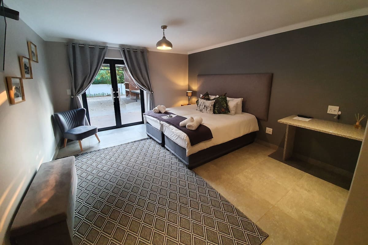 Una habitación de hotel moderna con cama, mesita de noche, silla y vistas al exterior por una puerta corredera.