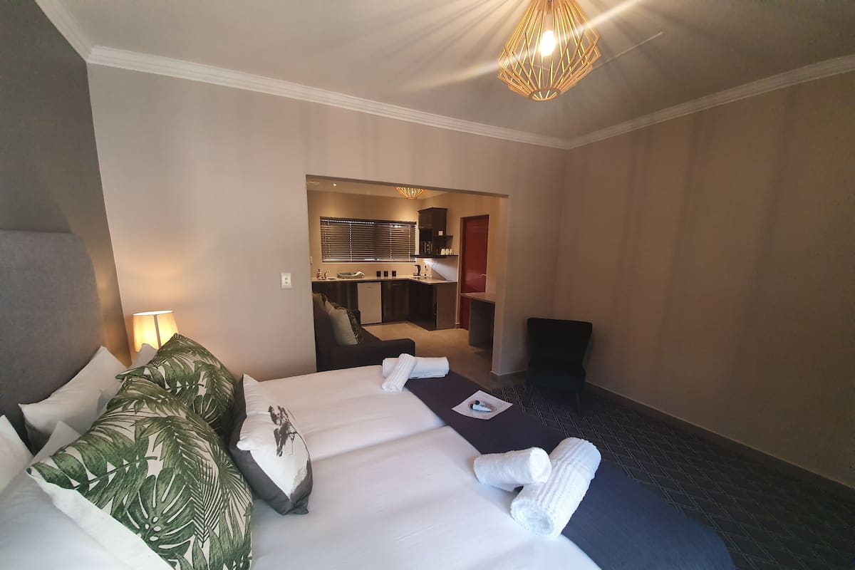 Una habitación de hotel con una cama grande, un escritorio, una silla y una kitchenette al fondo.