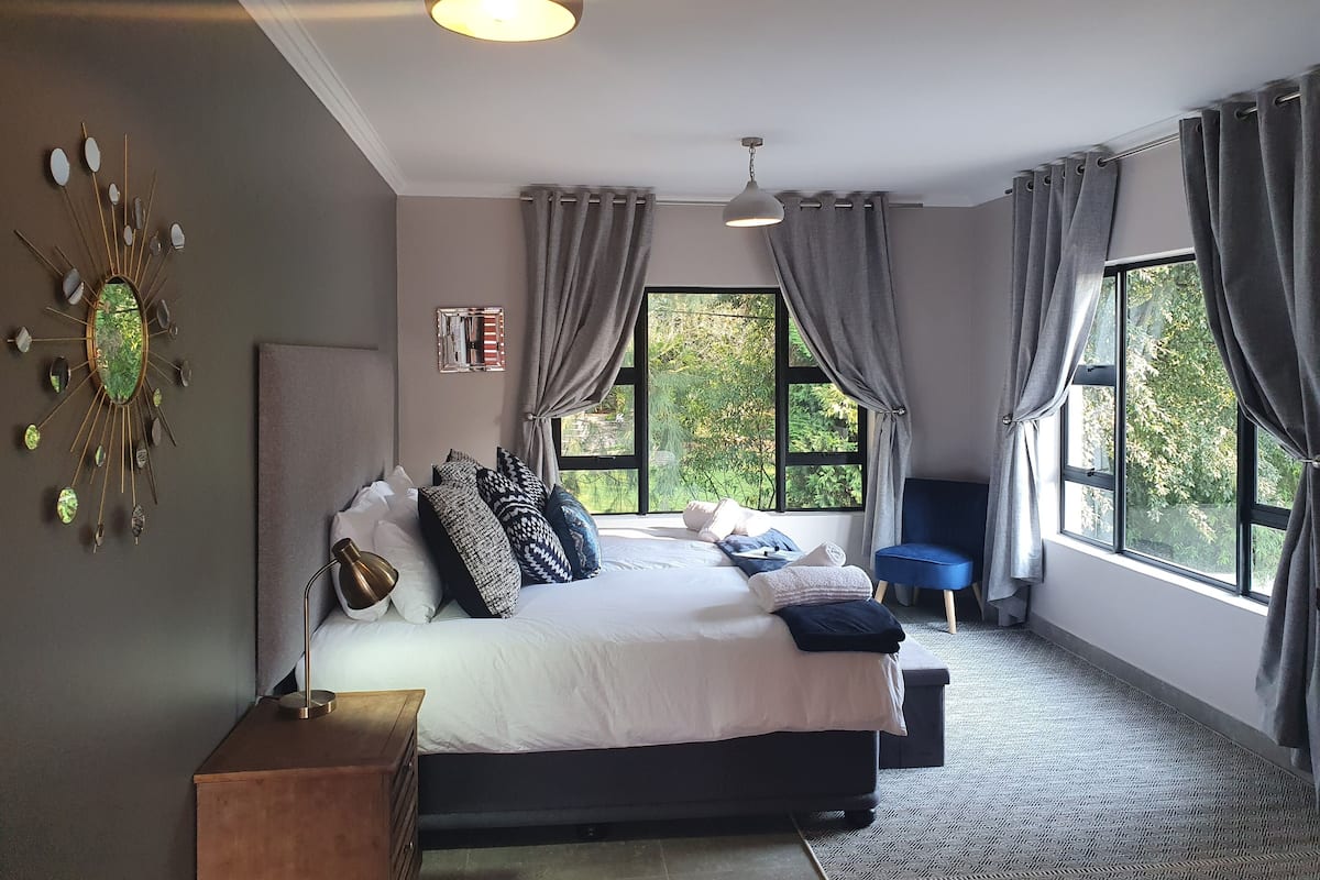 Un dormitorio con una cama grande, una mesita de noche, un espejo y una ventana con cortinas.
