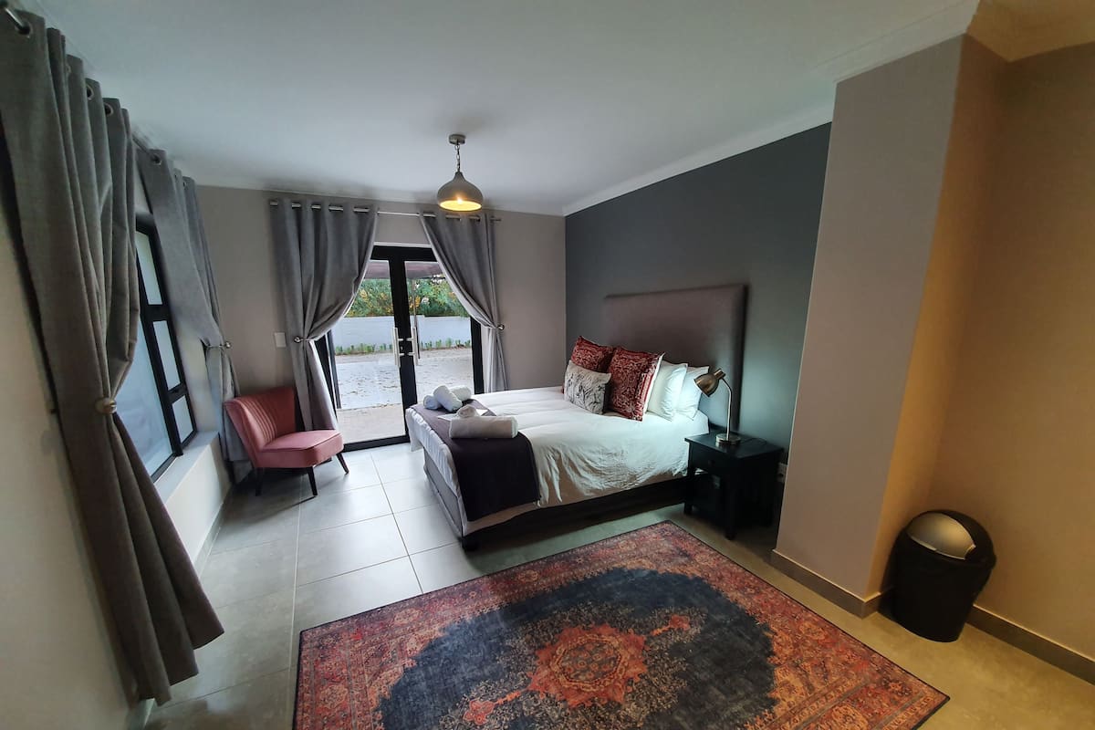 Un dormitorio moderno con cama, mesita de noche, silla, alfombra y vistas al exterior.