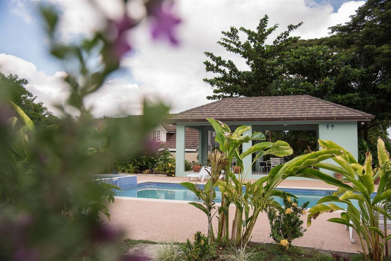 A pool area with a covered seating area and lounge chairs.