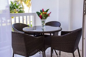 A round table with four dark wicker chairs, a glass vase with flowers, and a white railing in the background. - Seaside Condo 3 (Tower Isle)