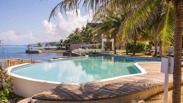 Ein Pool mit Holzterrasse, umgeben von Palmen und Blick auf das Meer.
