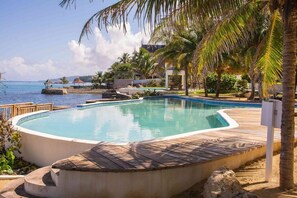 A pool with a wooden deck, surrounded by palm trees and a view of the sea. - Seaside Condo 3 (Tower Isle)