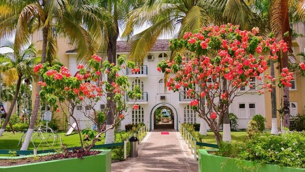 A pathway leading to a building with a central archway, surrounded by lush greenery and flowering trees. - Sunburst Studio Suite @ Sandcastles Resort (Ocho Rios)