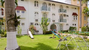 A hotel courtyard with a playground, palm trees, and a white building with balconies. - Sunburst Studio Suite @ Sandcastles Resort (Ocho Rios)