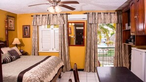 A hotel room with a bed, a desk, a chair, a ceiling fan, curtains, a window, and a view of the outside. - Sunburst Studio Suite @ Sandcastles Resort (Ocho Rios)