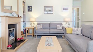Una sala de estar con chimenea, dos sofás, una mesa de centro y una estantería.