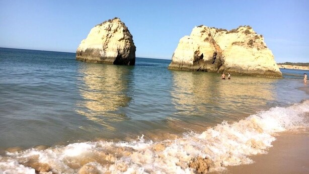 Una platja amb dues grans formacions rocoses i aigua transparent de color blau.