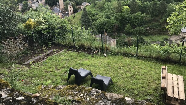 En landlig landsby med stenhuse, en stenvæg og et græsstykke med hegn og en skovl.