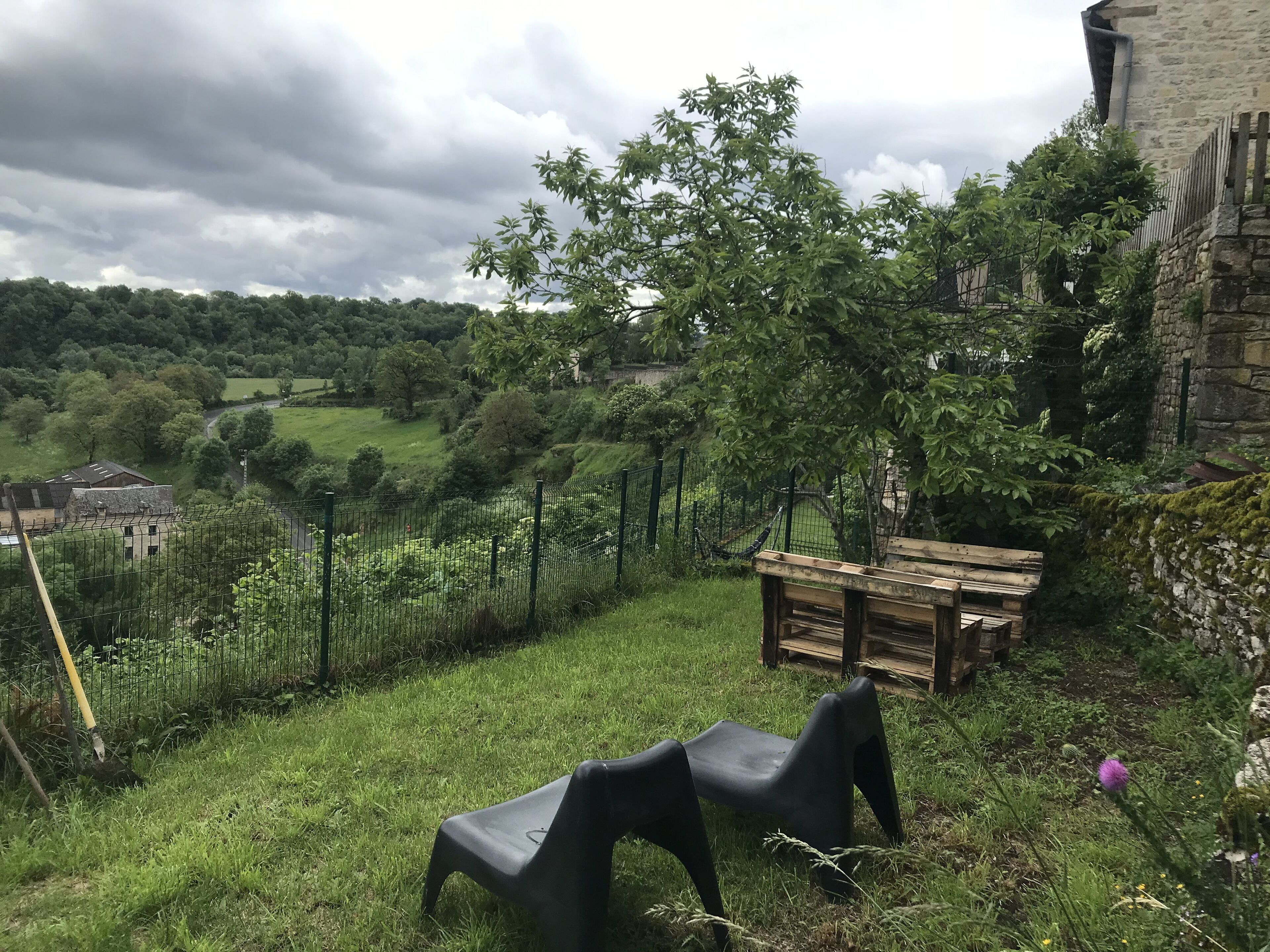 A rustic outdoor area with a wooden bench, a metal fence, and a grassy field.