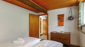 Ein Zimmer mit zwei Betten, einem Holzschrank, einem Spiegel und einer hängenden Pflanze.